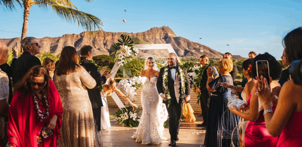 Bride and groom walking down the aisle at Leahi Room and Lanai after their wedding, smiling and looking at guests with Diamond Head in the background.