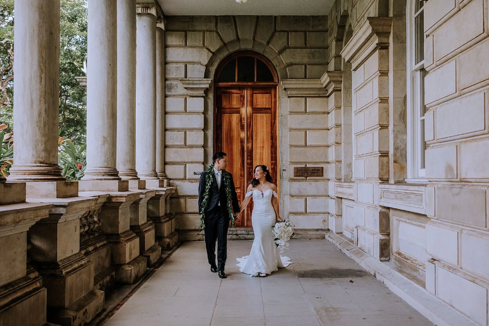 Bride and groom walking hand-in-hand on an ornate terrace during their Hawaii wedding, planned by Neu Events.