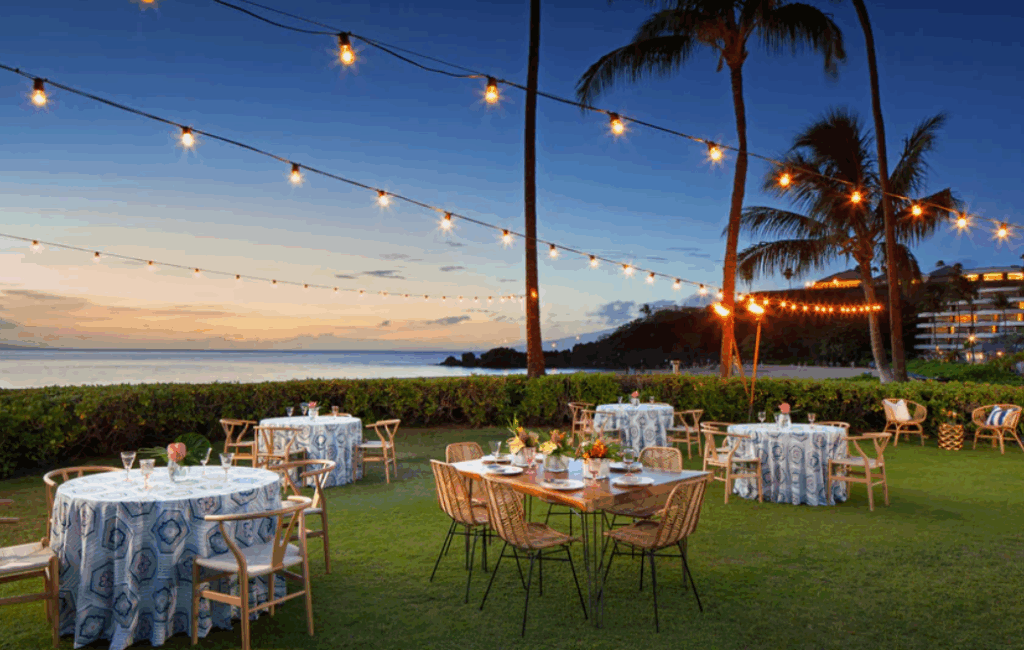 Outdoor wedding at dusk at Sheraton Maui with softly lit ceremony lawn, ocean backdrop, and Black Rock silhouette at sunset.