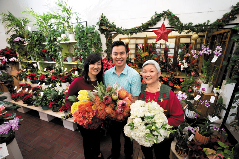 Three workers from Beretania Florists stand inside their flower shop holding fresh flowers.