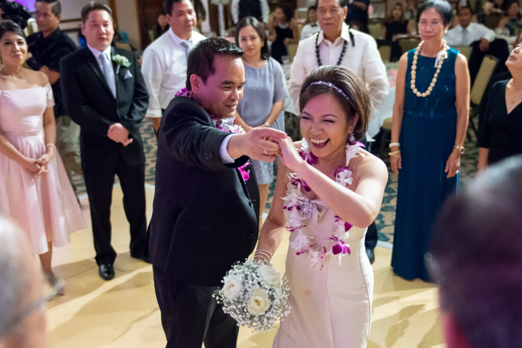 Bride dances with her groom on the dance floor in a color photo, surrounded by friends and family celebrating around them.