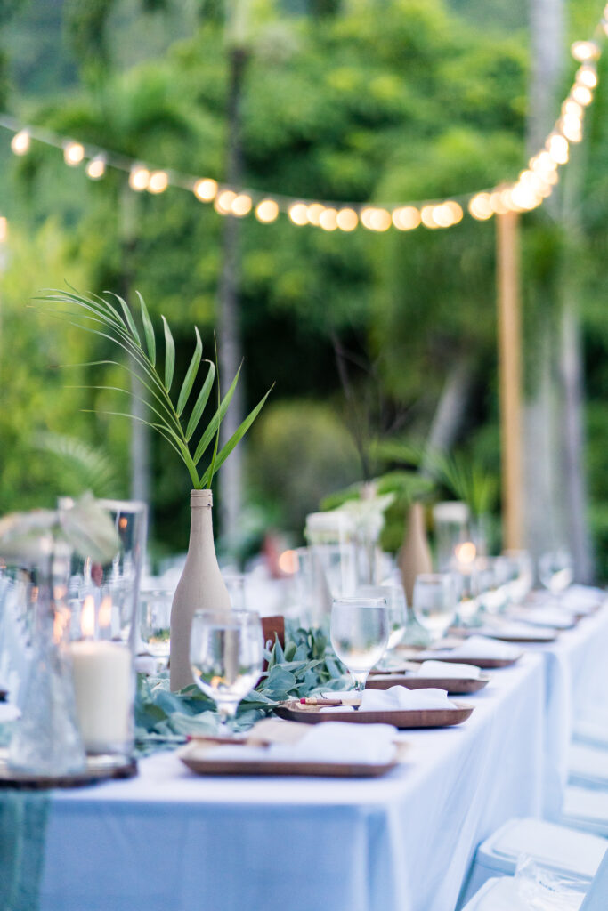 Tablescape outdoors in Hawaii with greenery and elegant candles lit.