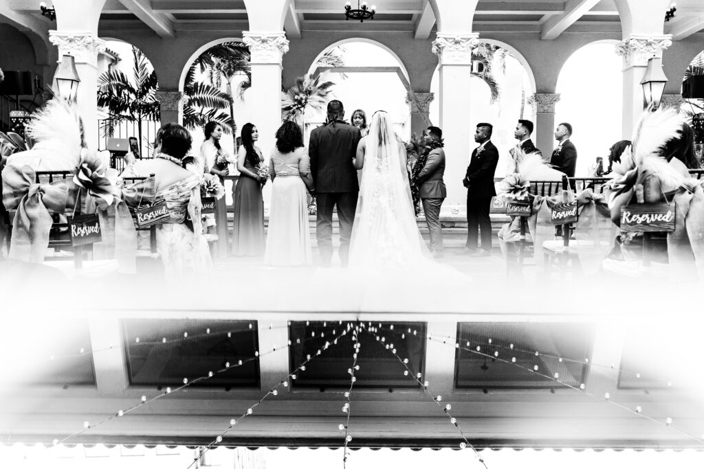 Black and white photo of a wedding ceremony at Café Julia, showing the couple at the altar with guests seated and the venue’s elegant architectural details in the background.