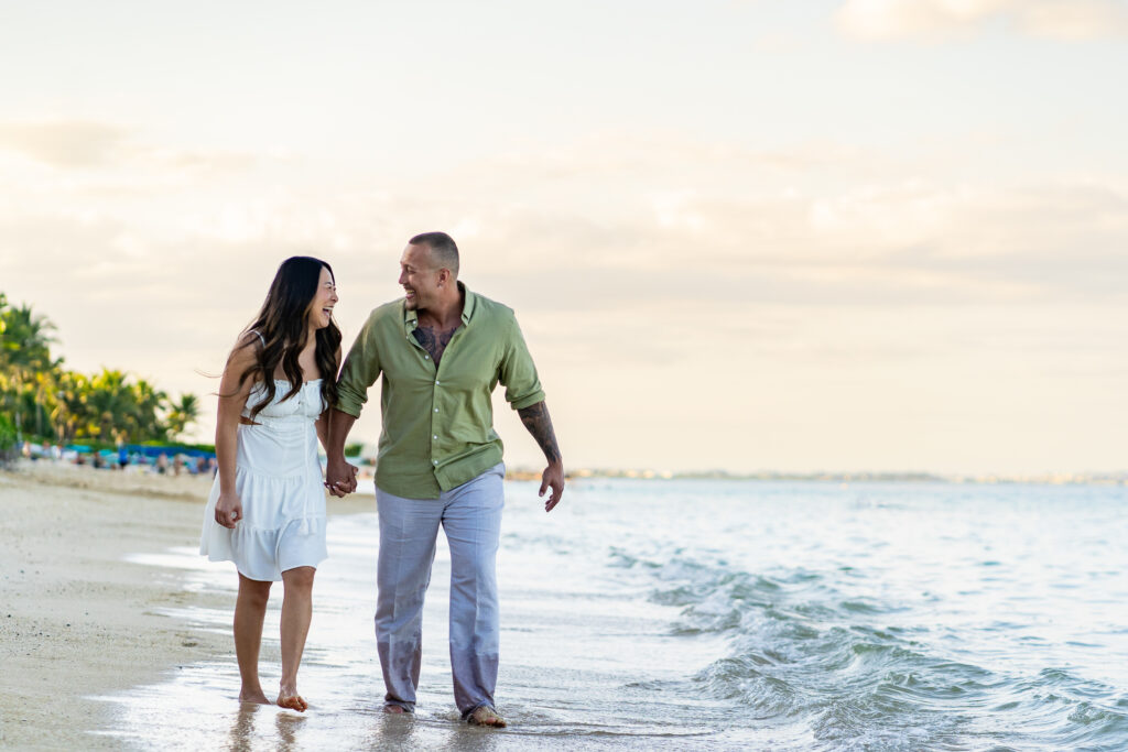 A newly eloped couple walks hand in hand through the waves along a Hawaiian shoreline.