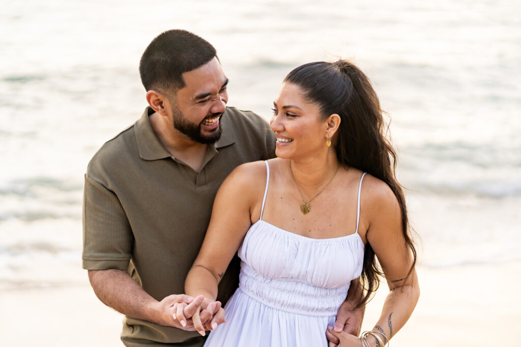 On the beach, the bride and groom laugh and look at each other during a relaxed, joyful moment.