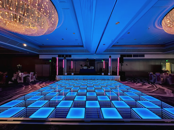 Oahu DJ setup by From Above Entertainment featuring a large blue illuminated infinity dance floor, DJ booth, uplighting, and ballroom chandeliers.
