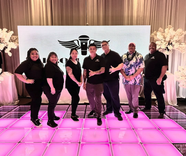From Above Entertainment team standing together on an illuminated wedding dance floor in front of their LED display after an Oahu wedding event.