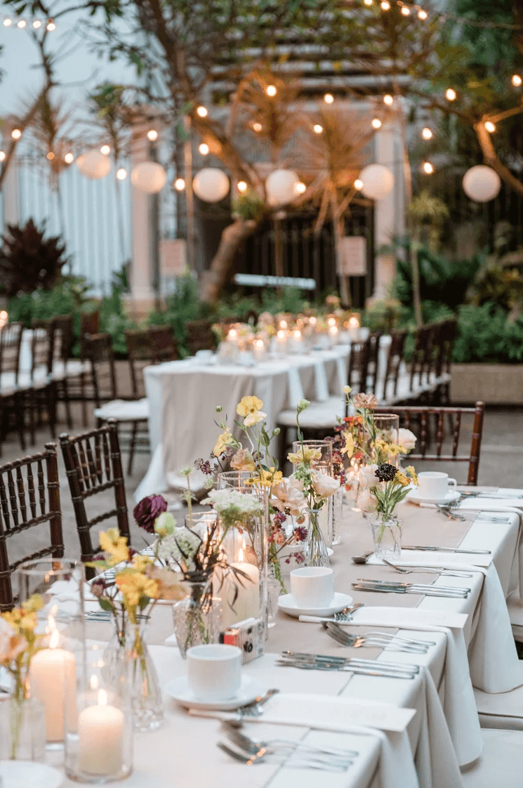 Wedding reception table from an Esselle Weddings coordinated celebration featuring blush and red roses, white hydrangeas, candles, rose gold flatware, and personalized place settings.