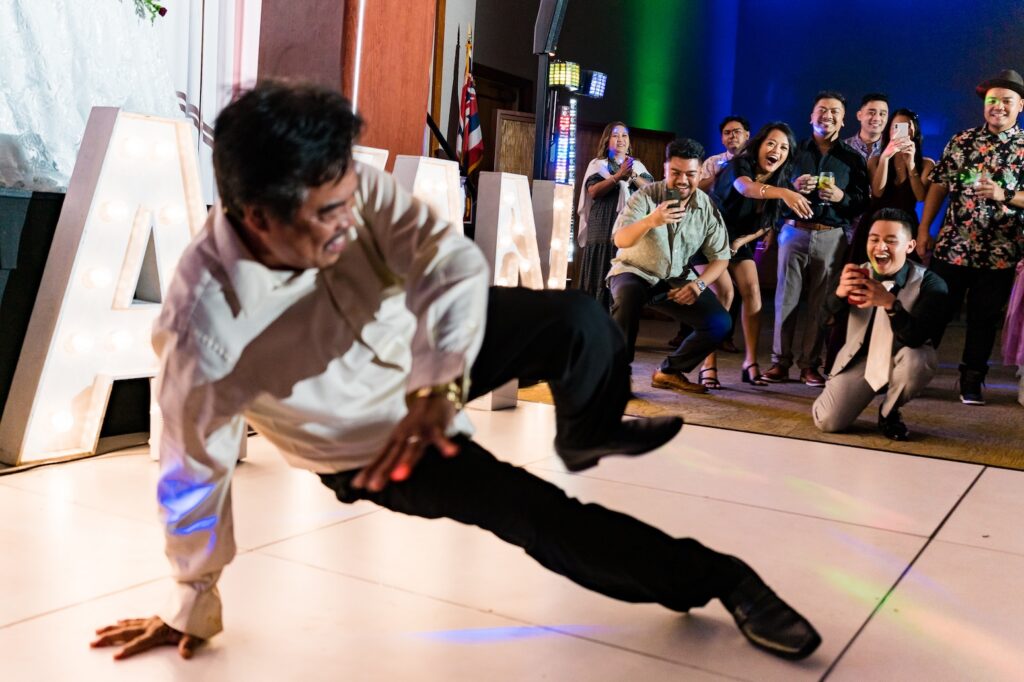 Energetic Oahu wedding dance floor photographed by Blessed Creatives, with a guest dancing as friends cheer under colorful DJ lighting during the reception.