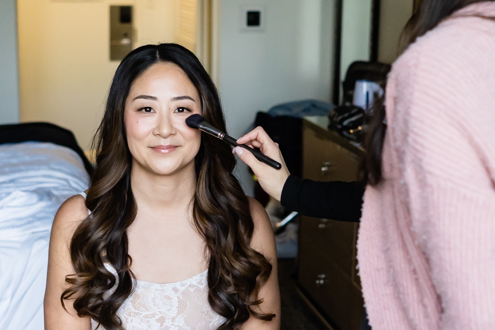 Makeup artist applying makeup to a bride while getting ready, illustrating how much to tip wedding vendors.